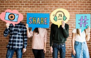 Some young people holding up social media icons in front of their faces (but they probably don’t own any social media stocks).