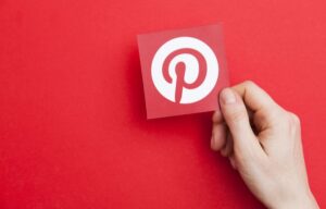 A hand holds up a Pinterest logo against a red background. Pinterest stock has done well in light of its recent earnings report.