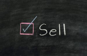 The word “sell” on a blackboard next to a marked checkbox. We’ll explain to you when to sell stocks as an investor.