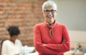 A woman in her 60s who is happy in an office since she has been building wealth.